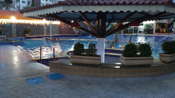 A swimming pool area with a covered seating area, tiled flooring, and potted plants. - Apartment for rent in Caldas Novas (Do Turista)