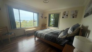 A bedroom with a large window, a bed, a bedside table, a chair, and a lamp. - 63 Vista Drive, Mallacoota (Mallacoota)