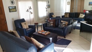 A living room with blue leather sofas, a coffee table with remote controls and magazines, and a television on a stand. - Beautiful Desert Princess Resort Condo Awesome Views of Golf Course & Mountains  (Cathedral City)