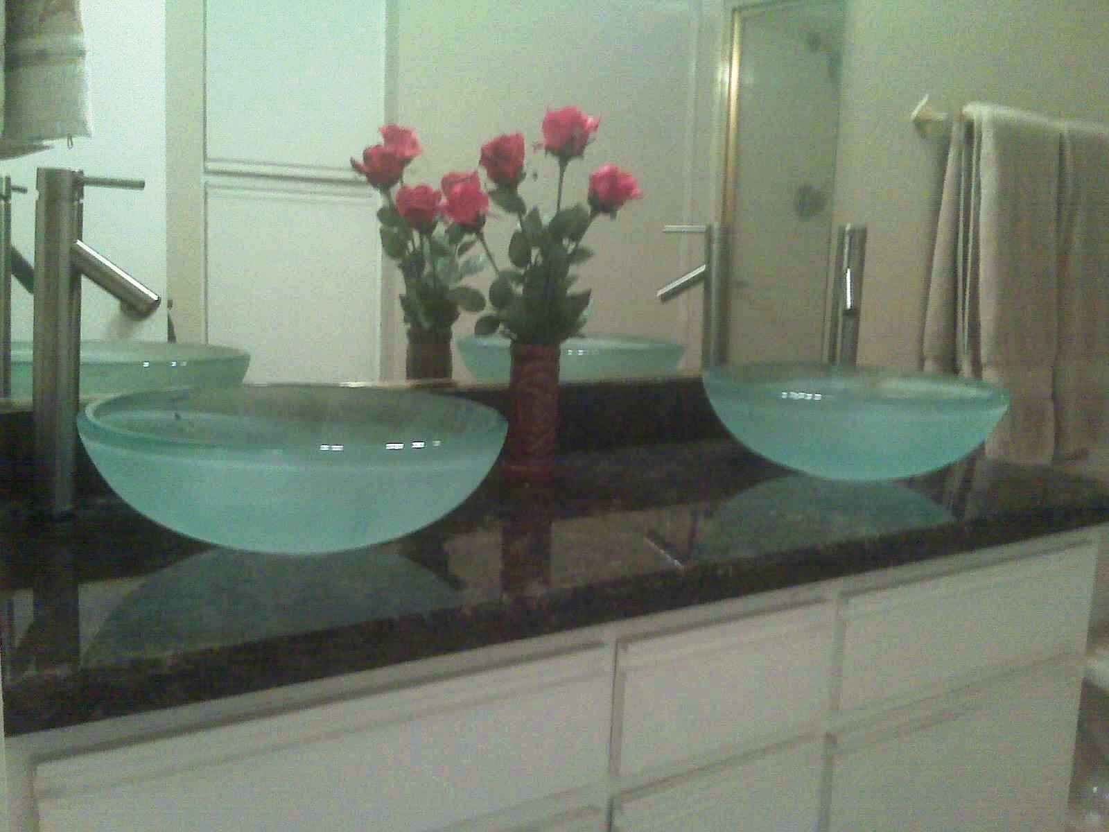 Un bagno con due grandi lavabi rotondi blu, uno specchio e un vaso con fiori rosa.