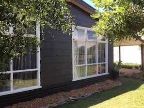A house with a dark exterior, white window frames, and a small garden area with mulch and grass.