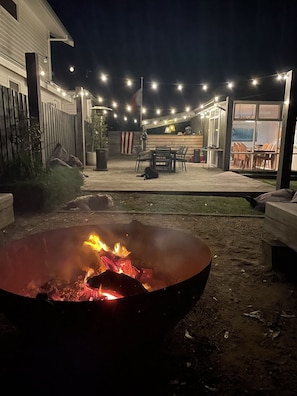 A backyard with a fire pit, outdoor seating, and string lights.
