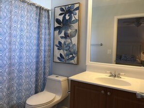 Un baño con inodoro, lavamanos con espejo superior y cortina de ducha con estampado floral.
