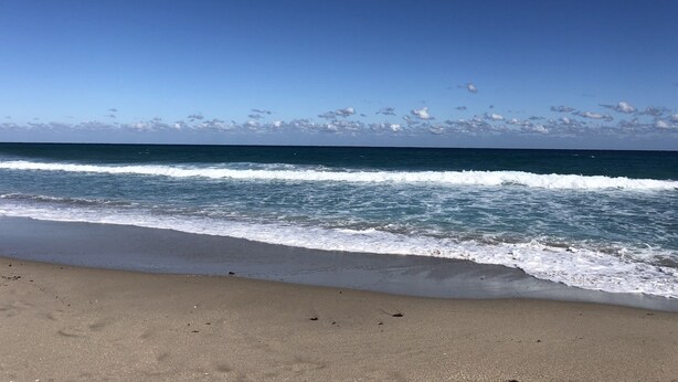En strand med vågor som rullar in mot land under en klar himmel.