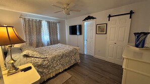 Un dormitorio con cama, ventilador de techo, televisión, puerta y cómoda.