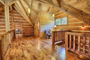 A spacious log cabin interior with a wooden floor, a staircase, and a window providing natural light.