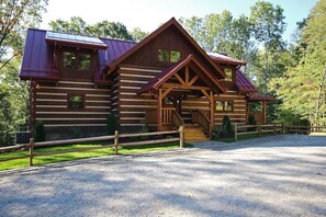A log cabin with a covered porch, a fenced yard, and a gravel driveway.