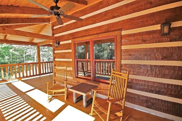 A wooden cabin with a porch, a ceiling fan, and a table with chairs.