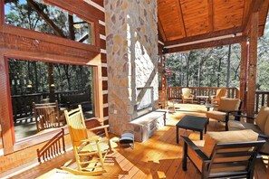 A wooden deck with stone pillars, outdoor seating, and a fireplace.