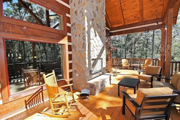 A wooden deck with stone pillars, outdoor seating, and a fireplace.