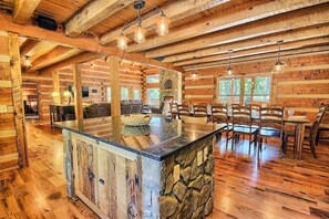 A spacious log cabin interior with a central island, stone accents, wooden furniture, and a fireplace.