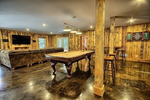 Una sala de billar con mesa de billar, taburetes de bar y dardos.