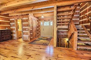 Ein Holzblockhaus-Innenraum mit einer Holztreppe, einer Haustür und einem kleinen Teppich auf dem Boden.