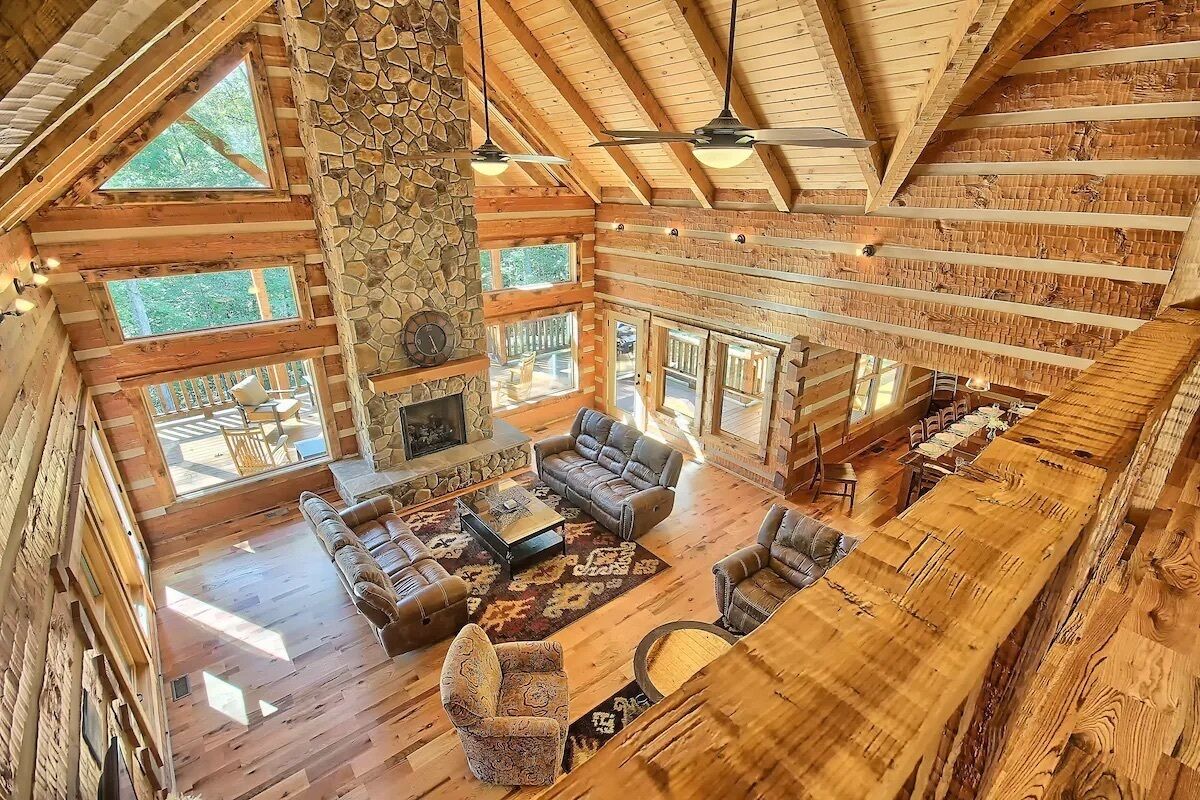 A spacious lodge with a high ceiling, stone fireplace, and large windows.