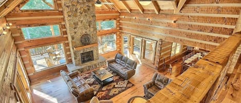 A spacious lodge with a high ceiling, stone fireplace, and large windows.