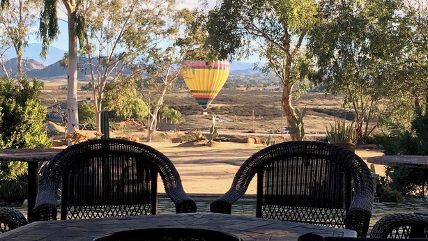 A patio with wicker chairs and a fire pit, overlooking a scenic landscape with trees and mountains. - Enjoy the RANCHO Villa Heart of Temecula Wine Country Golf Casinos Views RVC-023 (Temecula)