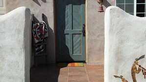 Un edificio intonacato con una porta verde, un piccolo portico e una scultura in metallo raffigurante una persona che tiene una pianta.