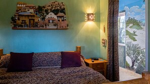 Una camera da letto con un letto, un comodino, una lampada a muro, un quadro e una finestra con vista sul paesaggio.