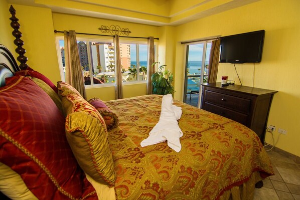 Een hotelkamer met een groot bed, een televisie en een balkon met uitzicht op zee.