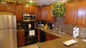Cozinha com armários de madeira, eletrodomésticos de aço inoxidável, bancadas de granito e painel de parede com folhagem verde.
