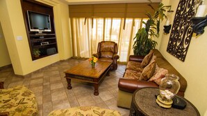 Uma sala de estar com TV, sofá de couro, mesa de centro e poltronas estampadas.