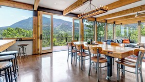 A spacious dining area with a large wooden table and chairs, large windows offering mountain views, and a modern chandelier. - Spectacular Views - Stunning Modern Broadmoor Home (Colorado Springs)