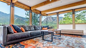 A modern living room with a leather sofa, a coffee table, and a patterned rug. Large windows offer a view of mountains and trees. - Spectacular Views - Stunning Modern Broadmoor Home (Colorado Springs)
