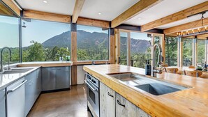 A modern kitchen with large windows, wooden beams, and a view of mountains. - Spectacular Views - Stunning Modern Broadmoor Home (Colorado Springs)