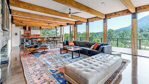 A spacious living area with a large sofa, coffee table, and a patterned rug. There is a kitchen in the background with a dining area. - Spectacular Views - Stunning Modern Broadmoor Home (Colorado Springs)