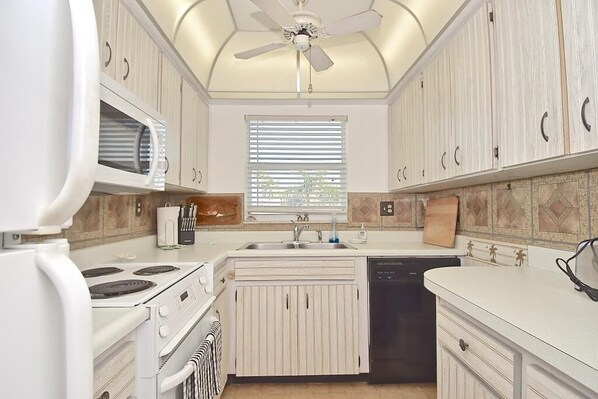 A compact kitchen with white cabinetry, a built-in microwave, a stove, a dishwasher, and a ceiling fan. - Waterfront withGreat Views, Heated Pool Overlooking the Bay, Quiet, Friendly Community #39 (Siesta Key)