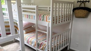 Un lit superposé avec une literie à rayures, un mur blanc et un panier tressé suspendu à un crochet.