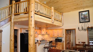 Ein großzügiger Wohnbereich mit einer Holztreppe, die zu einer oberen Ebene führt, eine Küche mit Holzausstattung und ein Essbereich mit einer Chandelüster.