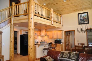 Cozy living area with a high ceiling and exposed beams, featuring a central staircase and a dining table for socializing.