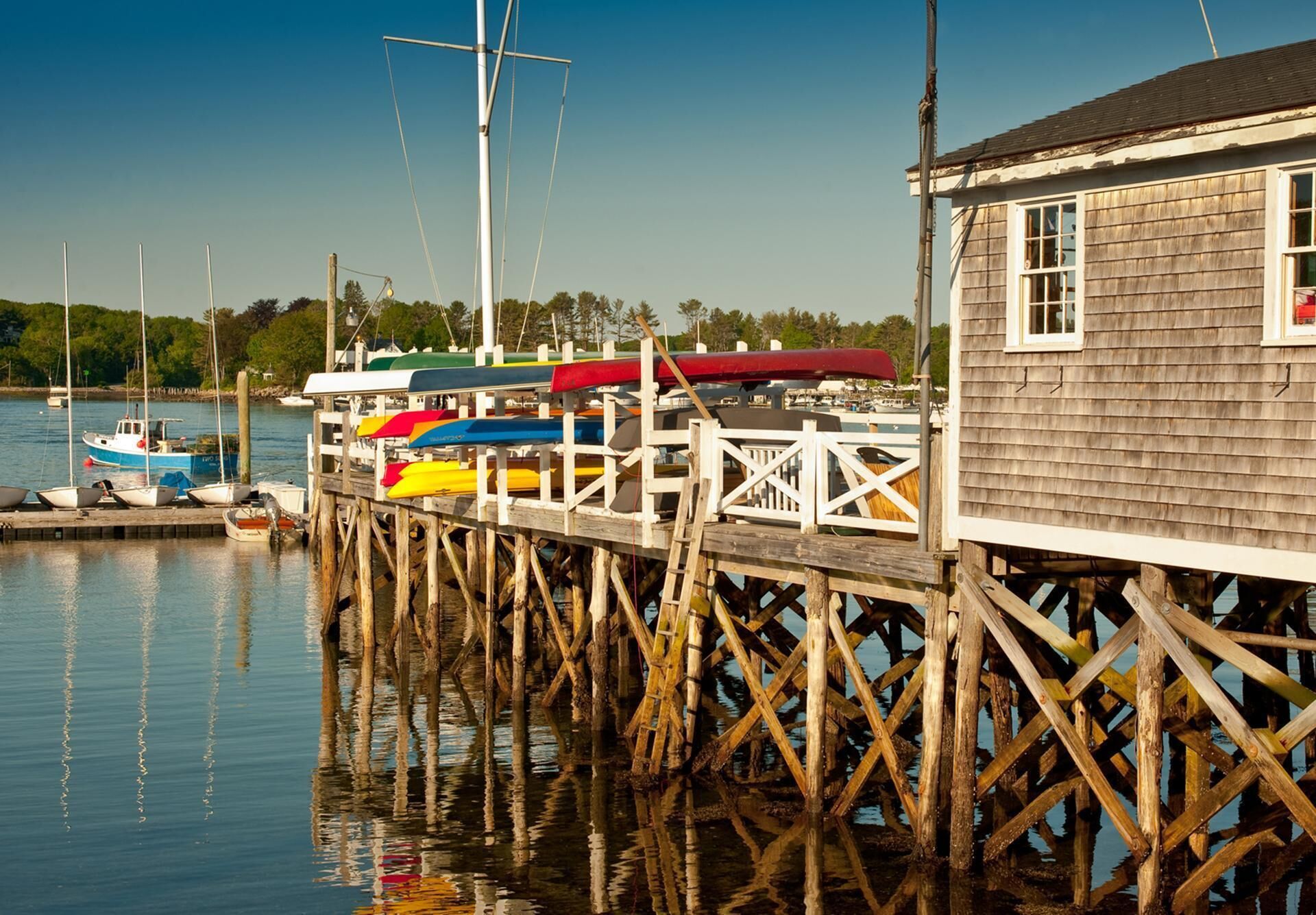 A wooden pier with a small building at the end, boats docked along the pier, and calm water reflecting the structure.