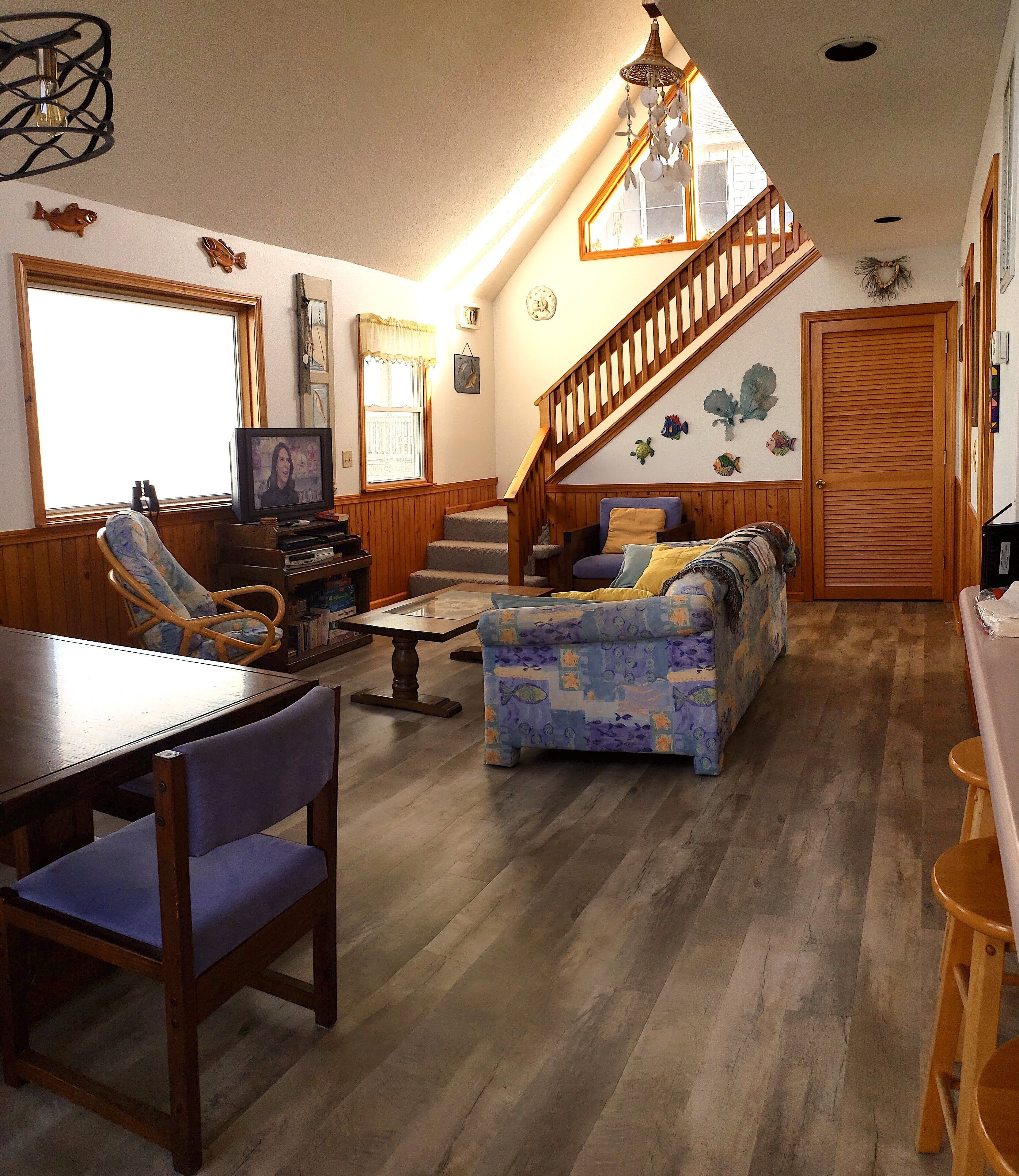 Ein gemütliches Wohnzimmer mit einer Holztreppe, einem Sofa, einem Fernseher und einem Essbereich mit Tisch und Stühlen.
