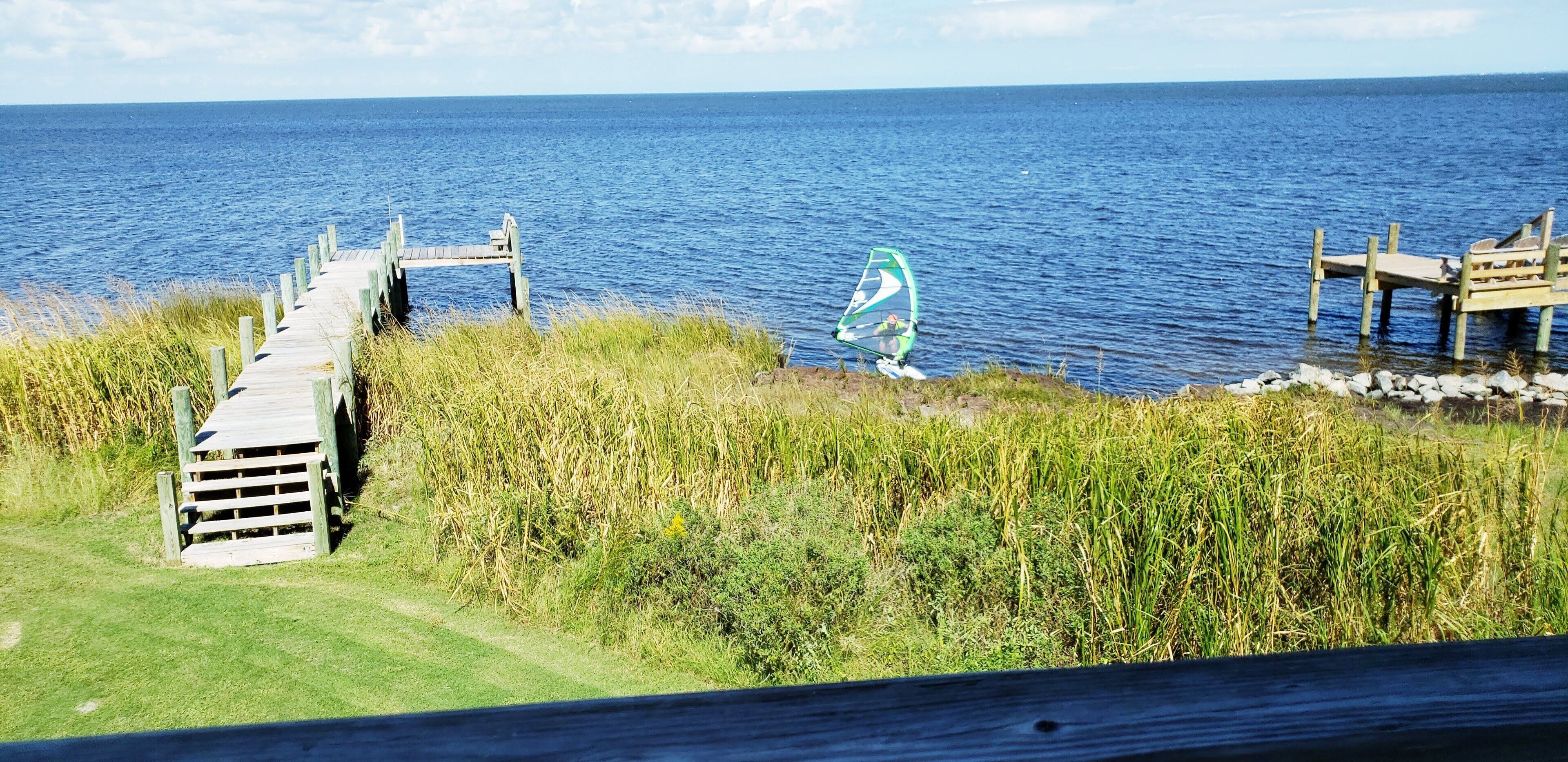 A wooden pier extending into a body of water, with a windsurfing board and rider visible.