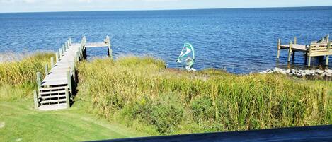 A wooden pier extending into a body of water, with a windsurfing board and rider visible.