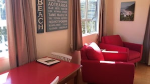 Una habitación con una mesa y una silla rojas, un sofá rojo, una ventana con cortinas y una pared con nombres de minerales.