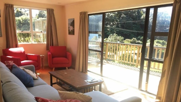 Una sala de estar con sofá, un sillón rojo y una mesa de centro. Hay un ventanal corredero que da a un balcón exterior.
