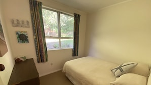 Un dormitorio con cama, ventana con cortinas, un escritorio pequeño e iluminación montada en la pared.