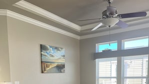 A modern living room with a sectional sofa, a ceiling fan, a painting, and large windows.