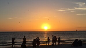 A sunset over a beach with people and a sailboat.
