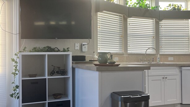 A modern kitchen with white cabinetry, a built-in TV, and a stainless steel trash can.