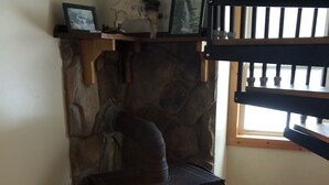 A stone fireplace with a wood-burning stove, a shelf with decorative items, and a window with blinds. - Rickett's Glen state Park!  Our cabin is only 1/2mile from the trail head. (Benton)