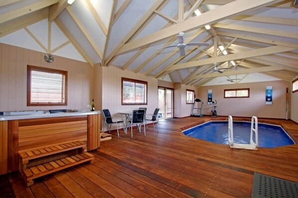 An indoor swimming pool with a wooden deck, a bar area, and exercise equipment.