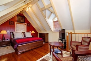 A bedroom with a sloped ceiling, a bed, a TV, and a seating area with chairs.