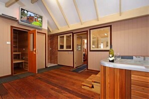 A room with a wooden floor, a built-in wooden bench, a television mounted on the wall, and a bar area with a bottle and glasses.
