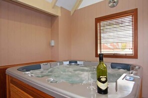 A hot tub with a bottle of wine and glasses, wooden panel walls, and a window with blinds. - Ocean Breeze Retreat - indoor pool, spa and sauna (Tootgarook)