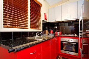 A kitchen with red cabinets, a stainless steel refrigerator, and a black countertop. - Ocean Breeze Retreat - indoor pool, spa and sauna (Tootgarook)