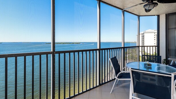 A balcony with a glass table and chairs, overlooking a body of water and a distant shoreline. - Sanibel Harbour Resort - Panoramic Beachfront Luxury 2/2 Condo! (Fort Myers)